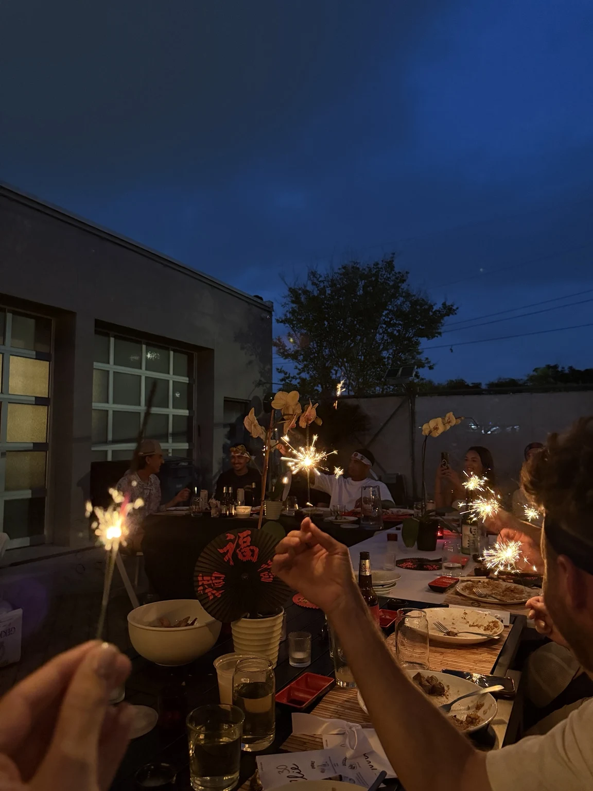 An outdoor group dinner with sparklers at dusk